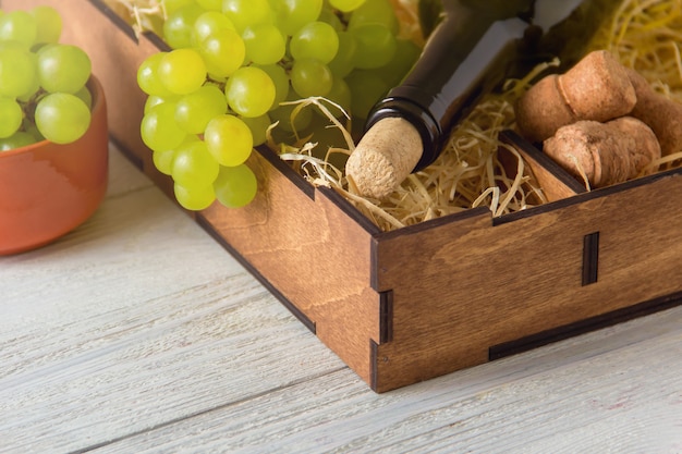 Botella de vino, corchos, uvas en caja de madera.