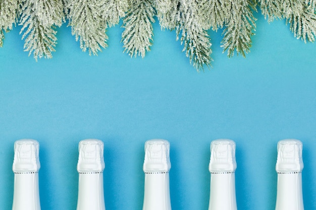 Botella de vino espumoso blanco y rama de árbol de Navidad verde sobre fondo azul Concepto de Navidad