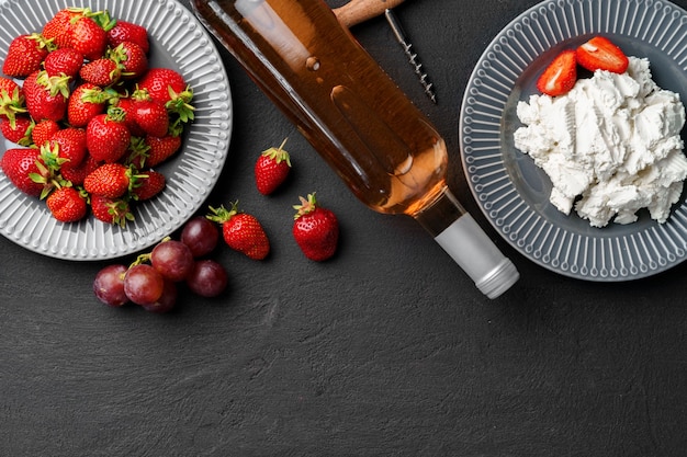 Botella de vino con fresas frescas y queso sobre superficie negra