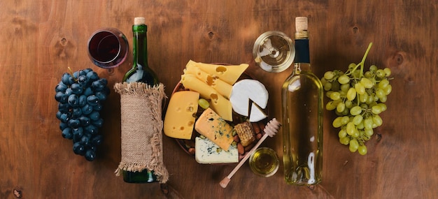 Una botella de vino y una gran variedad de quesos, miel, nueces y especias en una mesa de madera Vista superior Espacio libre para texto