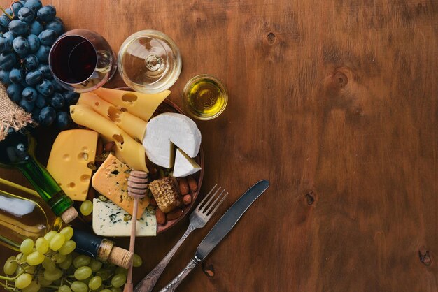 Una botella de vino y una gran variedad de quesos, miel, nueces y especias en una mesa de madera Vista superior Espacio libre para texto