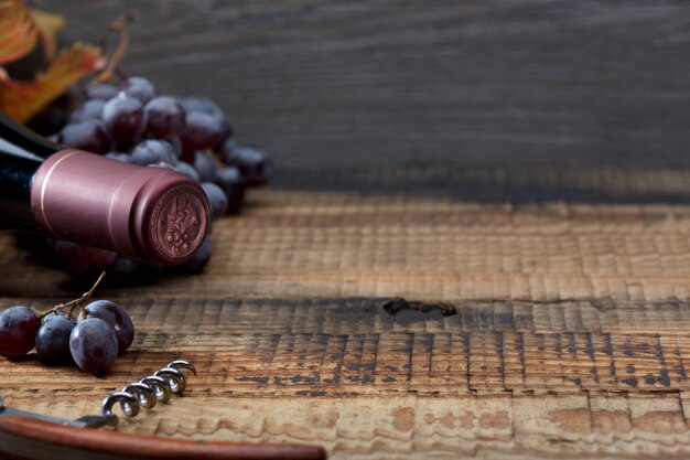 Botella de vino, racimo de uvas y hojas de parra en una vieja mesa de madera.