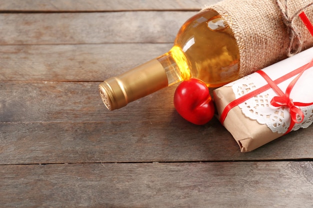 Una botella de vino y un regalo en la caja, sobre fondo de madera