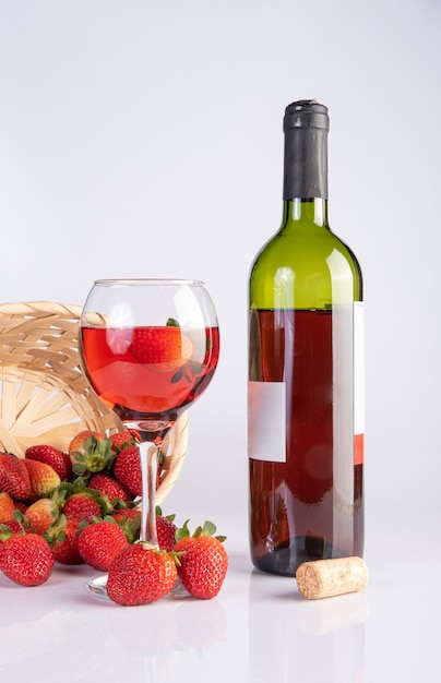 Botella de vino rosado y una copa de cristal junto con hermosas fresas sobre una superficie blanca, enfoque selectivo.