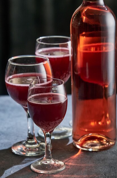 Una botella de vino rosado con tres vasos sobre una mesa de piedra.