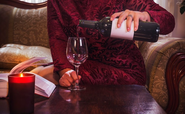 Botella de vino sirviendo una copa de vino tinto por una mujer latina