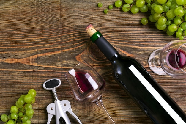 Botella de vino tinto, chocolate de uva y vasos sobre la vista superior de la mesa de madera con espacio de copia