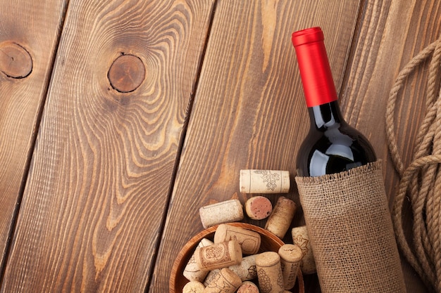 Botella de vino tinto y corchos sobre fondo de mesa de madera