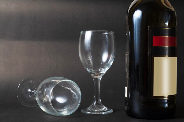 Foto botella de vino tinto y dos vasos de vino vacíos sobre un fondo negro