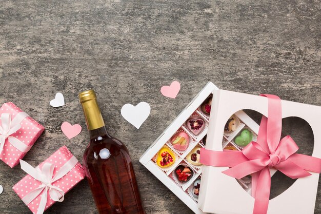 Botella de vino tinto en fondo coloreado para el Día de San Valentín con regalo y chocolate en forma de corazón con caja de regalos de chocolates vista superior con espacio de copia