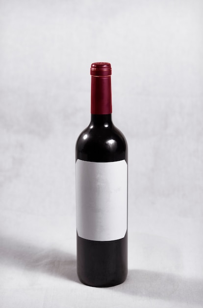 Botella de vino tinto oscuro con tapón rojo y etiqueta blanca sin letras ni marcas.