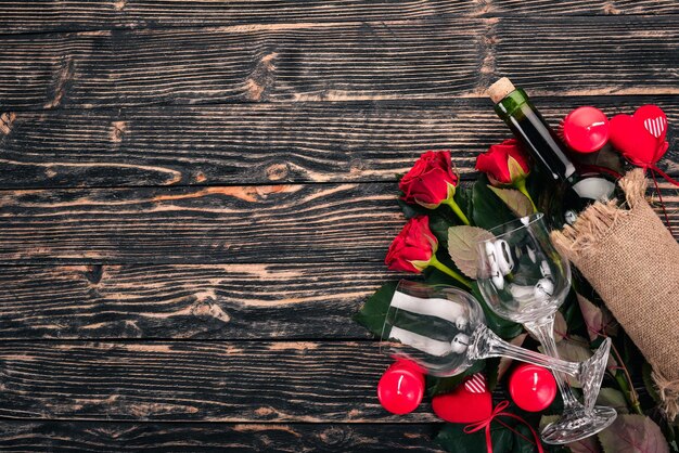 Una botella de vino tinto y un ramo de rosas rojas. Día de San Valentín. Sobre un fondo de madera. Vista superior. Espacio libre para su texto.