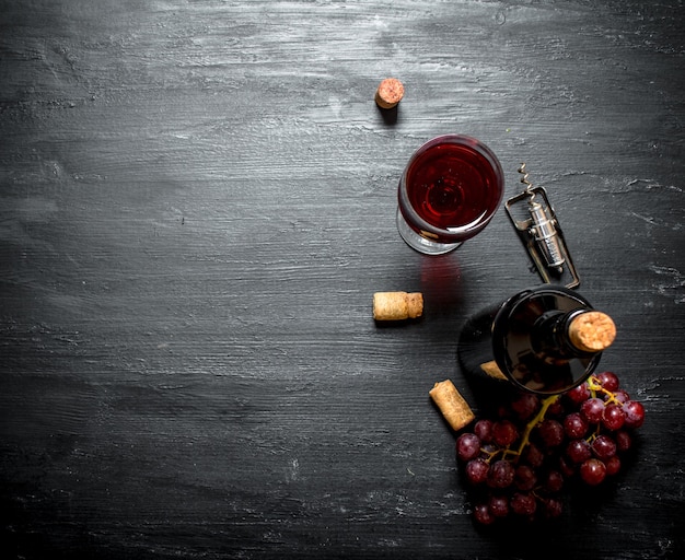 Botella de vino tinto con sacacorchos. Sobre un fondo de madera negra.