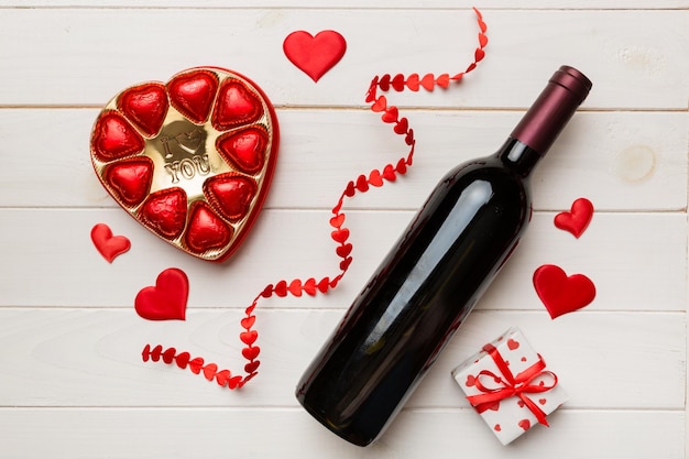 Botella de vino tinto sobre fondo de color para el Día de San Valentín con regalo y chocolate en forma de corazón con caja de regalo de chocolates vista superior con espacio de copia