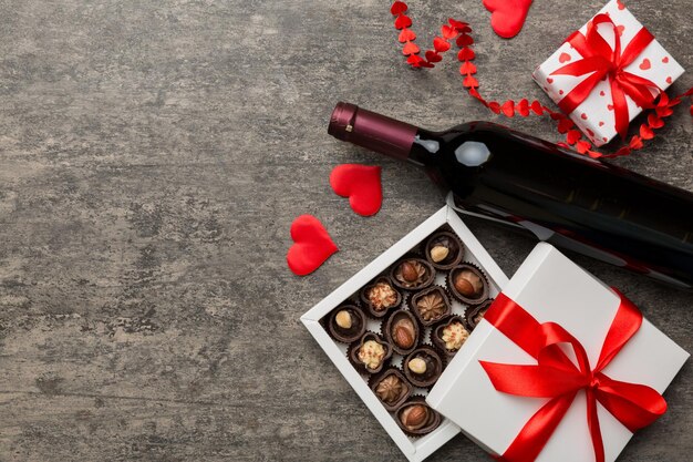 Botella de vino tinto sobre fondo de color para el Día de San Valentín con regalo y chocolate en forma de corazón con caja de regalo de chocolates vista superior con espacio de copia