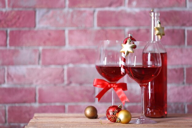 Botella de vino tinto y vasos con regalos de Navidad en la superficie de la pared