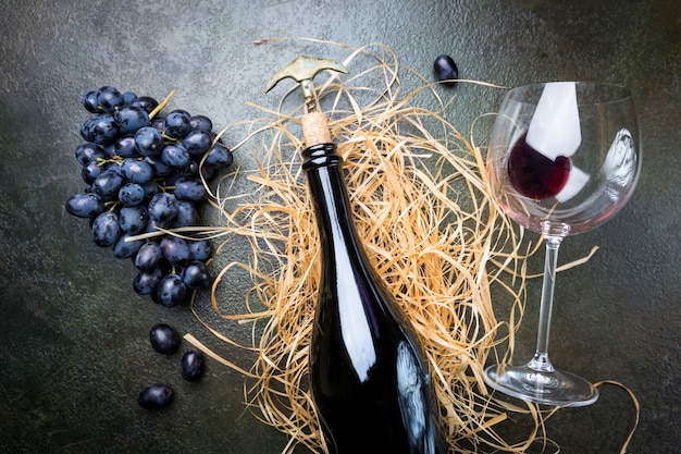 Una botella de vino tinto con vidrio y uvas sobre piedra oscura