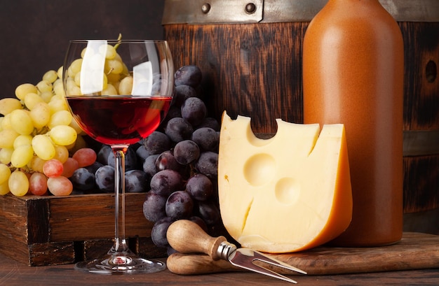 Botella de vino uvas queso vaso de vino tinto y viejo barril de madera