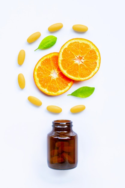 Botella de vitamina C y pastillas con fruta naranja sobre blanco