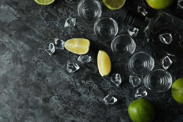 Botella de vodka, chupitos, cubitos de hielo y rodajas de limón en la mesa ahumada negra