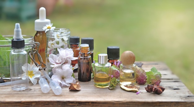 Botellas de aceite esencial con equipo de plantas y flores y aromaterapia en una mesa de madera en el jardín