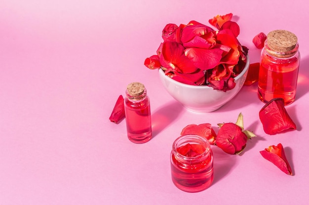 Botellas de aceite esencial y pétalos de rosas sobre fondo rosa. Luz dura de moda, sombra oscura, vista superior