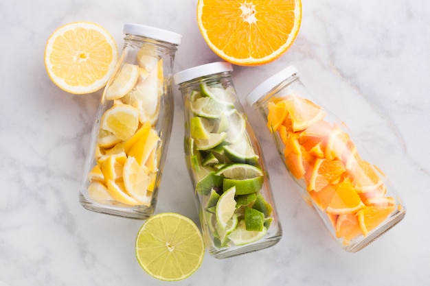 Botellas de agua fresca de verano con naranjas con limas y rodajas de limones en mármol con frutas frescas