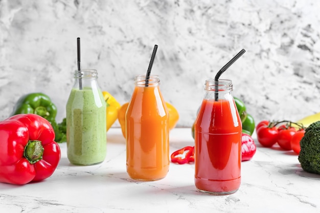 Botellas de batido saludable con diferentes verduras en superficie ligera