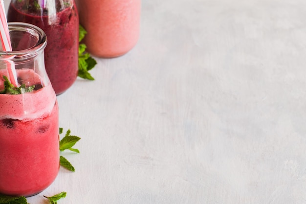 Botellas de batido sobre fondo blanco. Bebidas de frutas de fresa, cereza y bayas de vino con refresco de menta en el período de verano. Comida saludable de desintoxicación. Cerrar la imagen con espacio libre a la derecha.