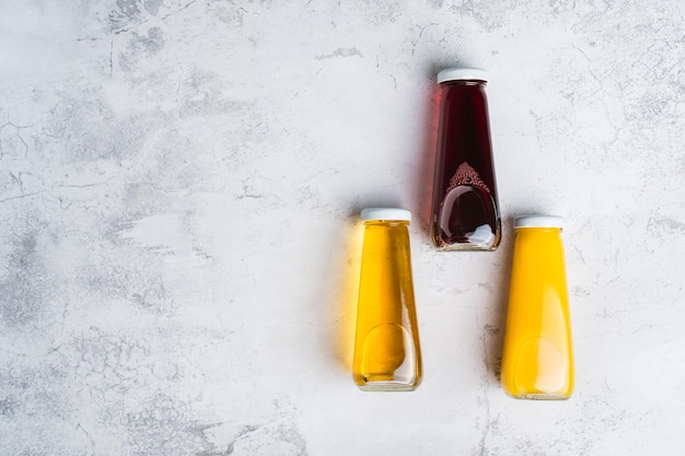 Botellas con bebida líquida amarilla y roja sobre fondo gris Jugo de cereza de manzana naranja