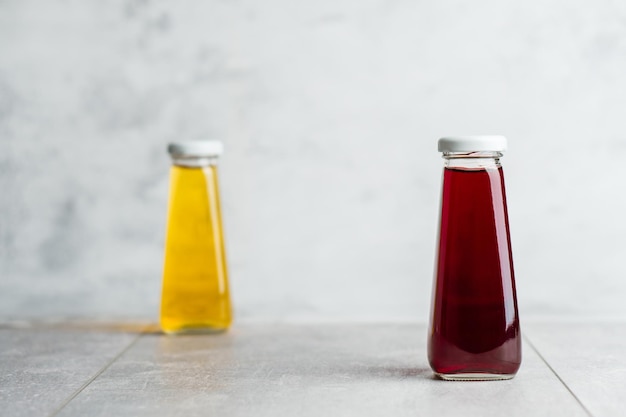 Botellas con bebida líquida amarilla y roja sobre fondo gris Jugo de naranja y cereza