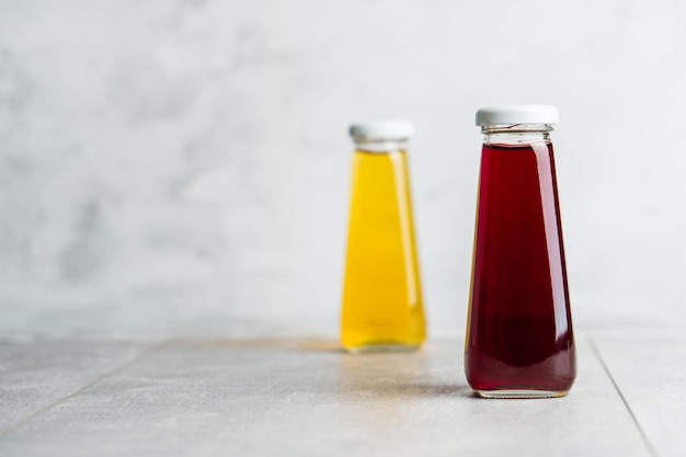 Botellas con bebida líquida amarilla y roja sobre fondo gris Jugo de naranja y cereza