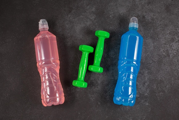 Foto botellas de bebidas energéticas con diferentes sabores y pesas sobre un fondo oscuro