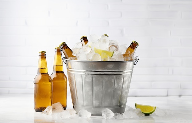 Botellas de cerveza en una canasta de metal con cubitos de hielo sobre un fondo claro para una bebida de fiesta