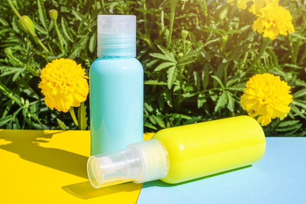 Foto botellas de cosméticos amarillas y azules en espacios del mismo color. las flores amarillas están detrás. concepto elegante de esencias orgánicas, belleza natural y productos para la salud.