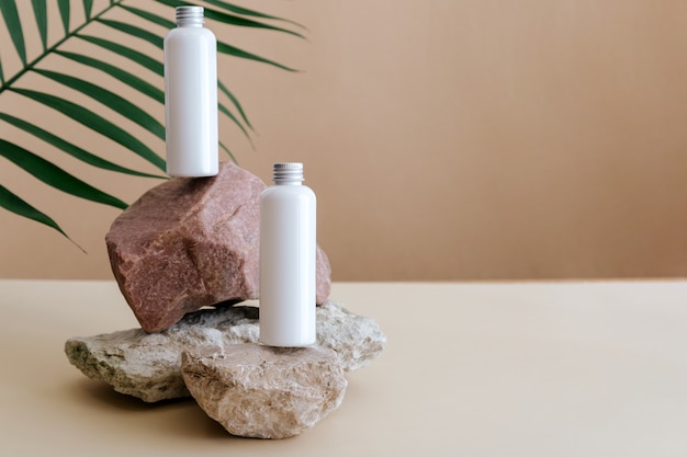 Botellas de cosméticos de belleza natural, producto cosmético de maqueta blanca para el cuidado de la piel en pedestal de piedra con hojas de palma. Botellas de loción blanca composición cosmética minimalista en el espacio de copia de fondo beige.