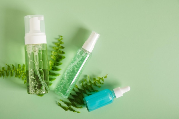 Botellas de cosméticos y hojas frescas de helecho sobre fondo verde Cosméticos orgánicos Maqueta de marca de cosméticos SPA