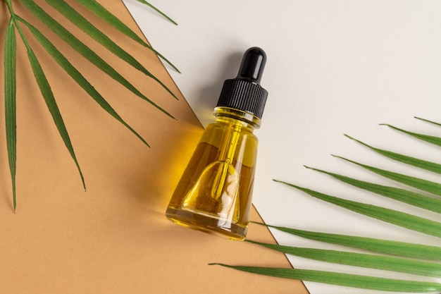 Botellas de cosméticos de vidrio con un gotero en una pared de color beige con hojas tropicales. Concepto de cosmética natural, aceite esencial natural.