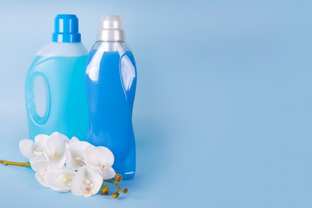 Botellas de detergente y suavizante con flores de orquídeas sobre fondo azul.