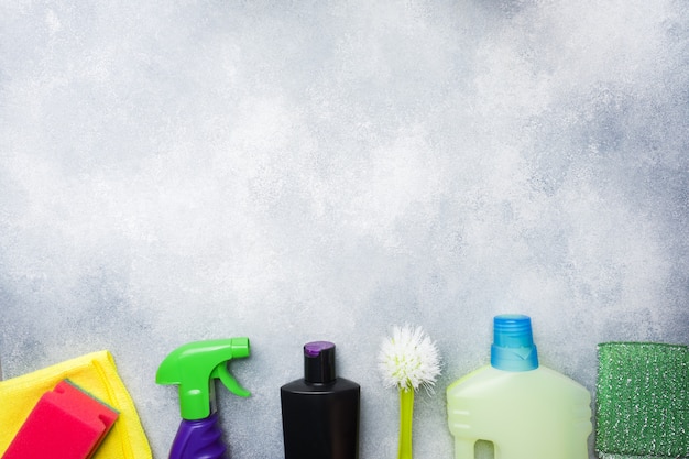 Botellas con detergentes, cepillos y esponjas sobre fondo de hormigón.