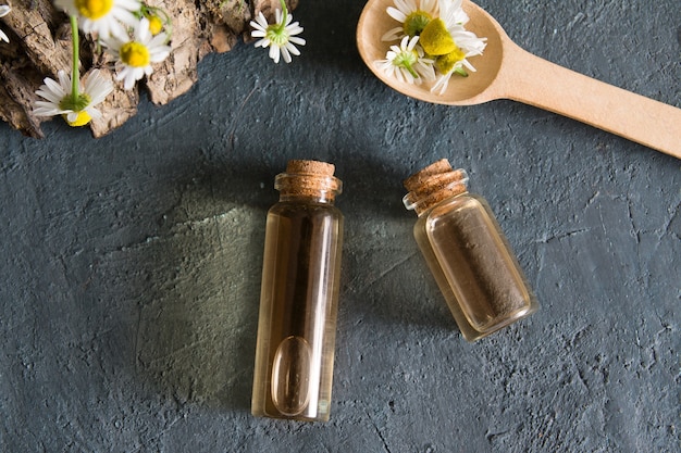 Botellas con esencia y manzanilla plana yacen sobre una superficie oscura.