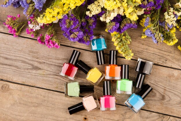 Botellas de esmalte de uñas de colores y flores en la mesa de madera marrón