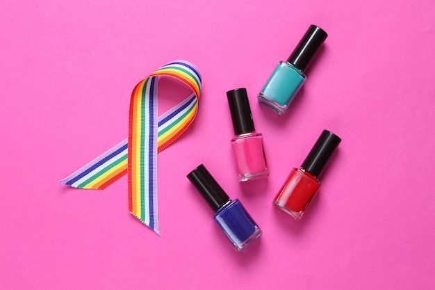 Botellas de esmalte de uñas y símbolo de cinta de orgullo de cinta de arco iris LGBT sobre fondo rosa Vista superior