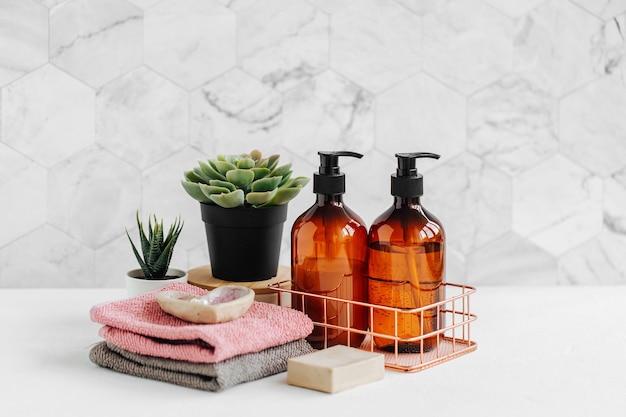 Foto botellas de jabón y champú y toallas de algodón con planta verde en el cuadro blanco dentro de un fondo de baño.