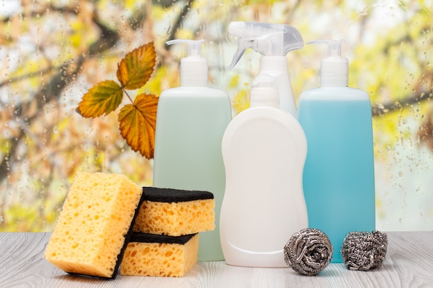 Botellas de líquido para lavar platos y esponjas frente a la ventana con gotas de agua.