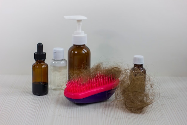 Botellas de medicamentos y cepillo para el cabello en la mesa de madera blanca Problema de pérdida de cabello