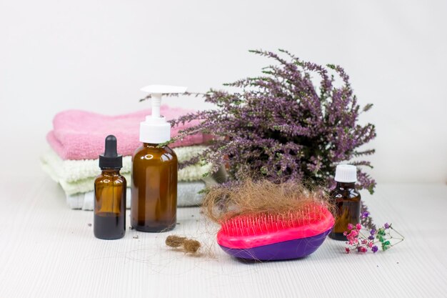 Botellas de medicamentos toalla cepillo para el cabello y brezo de hierbas en la mesa de madera blanca Problema de pérdida de cabello