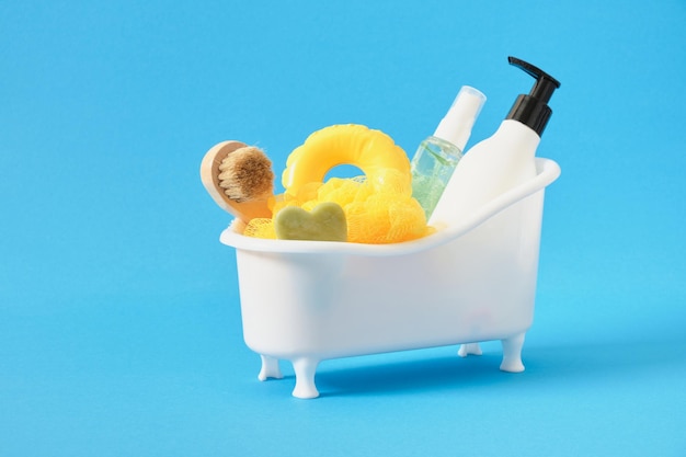Botellas en miniatura de baño de plástico blanco con toallita cosmética, cepillo de masaje con raspador gua sha y círculo pequeño para nadar, baño de fondo azul y concepto de cuidado corporal