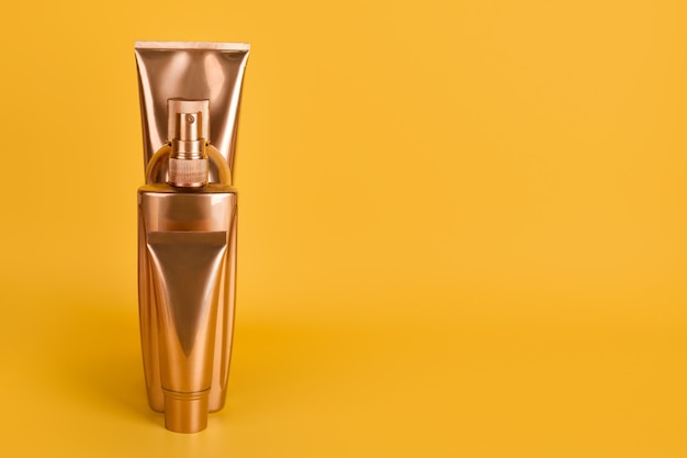 Botellas de oro, productos cosméticos en superficie amarilla.