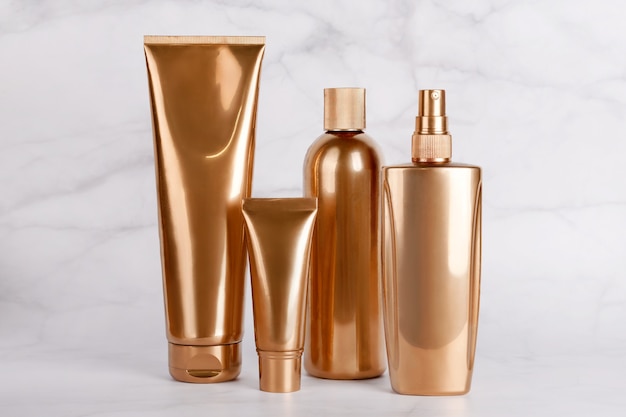 Botellas de oro, productos cosméticos en superficie de mármol.